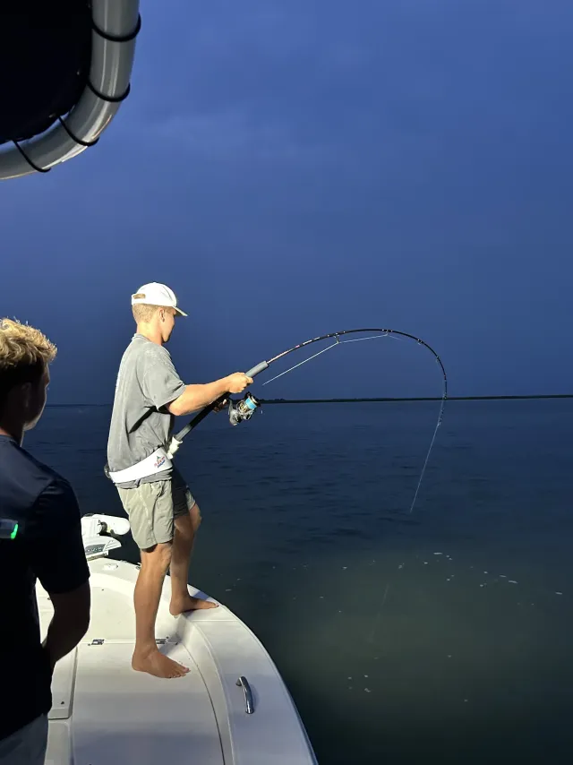 Angler fighting a shark at night from the bow of the boat